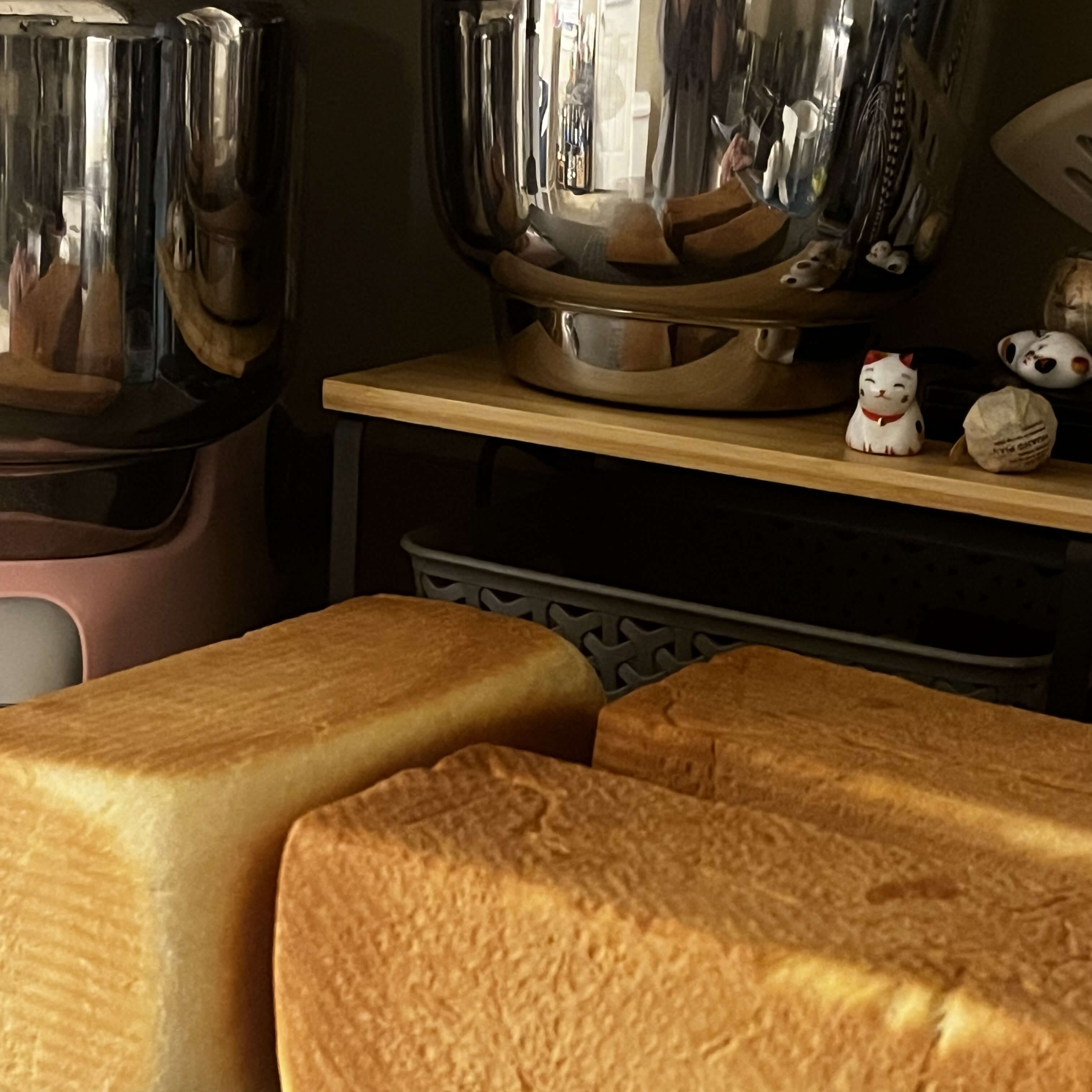 A countertop with a mixes, some bowls, and a cooling rack holding three loaves of bread.